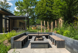 Udendørs opholdsområde med bænke og bålplads ved Loevestein Deluxe-lodge på Veluwepark de Bosgraaf i Holland.