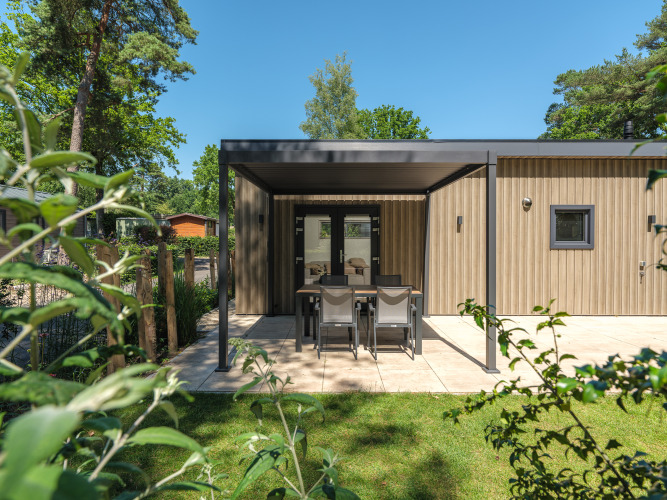 Moderne Holzhütte mit überdachter Terrasse, Essbereich und Garten, umgeben von Bäumen und Natur.