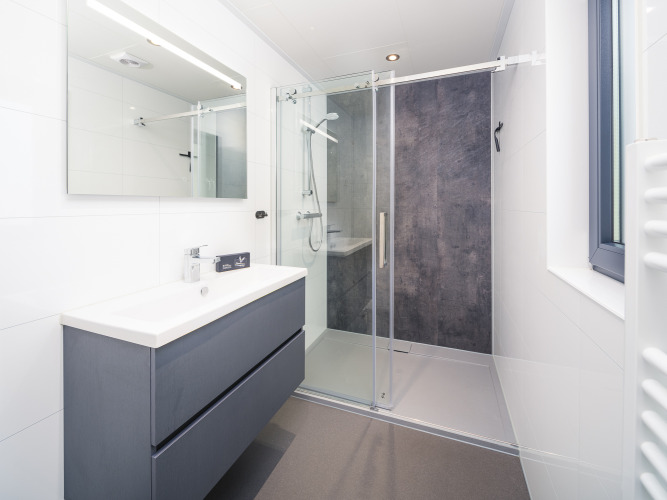 Modernes Badezimmer mit Dusche, großem Spiegel und Waschbecken in einer Lodge im Veluwepark de Bosgraaf, Niederlande.