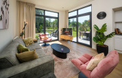 Modern lodge living room with large windows, soft seating, houseplants, and view of the garden.
