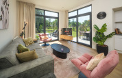 Sala moderna de alojamiento con grandes ventanas, sillones cómodos, plantas y vista al jardín.