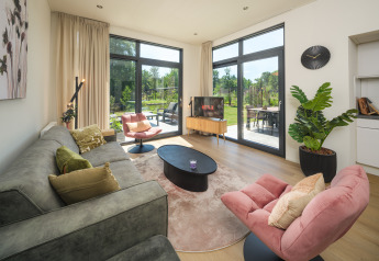 Modernes Lodge-Wohnzimmer mit großen Fenstern, gemütlichen Sesseln, Pflanzen und Gartenblick.