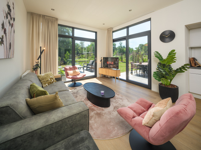 Modernes Lodge-Wohnzimmer mit großen Fenstern, gemütlichen Sesseln, Pflanzen und Gartenblick.