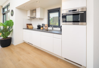 Moderne glampingtkeuken met witte kasten, ingebouwde oven, zwart werkblad en grote ramen met uitzicht.