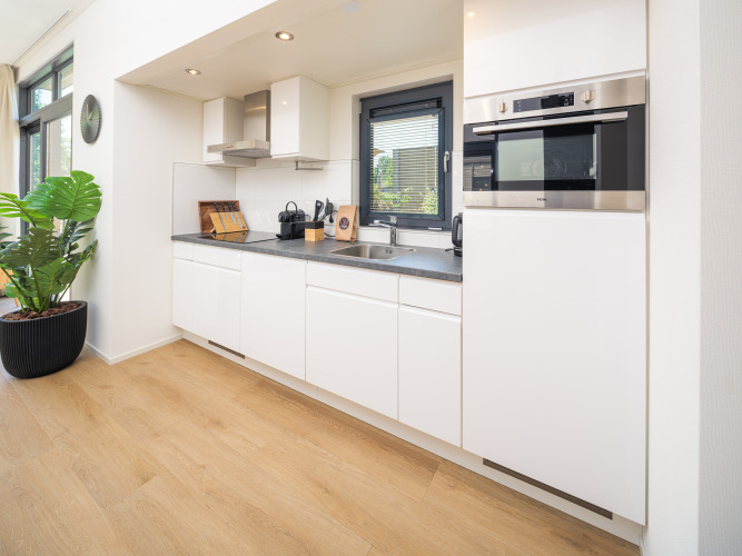 Modernes Glamping-Küche mit weißen Schränken, integriertem Backofen, großen Fenstern und Holzboden.