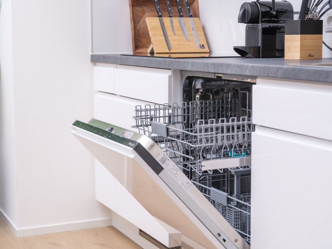 Moderne Glampingküche mit offener Einbau-Geschirrspülmaschine, bereit für Geschirr und Besteck.