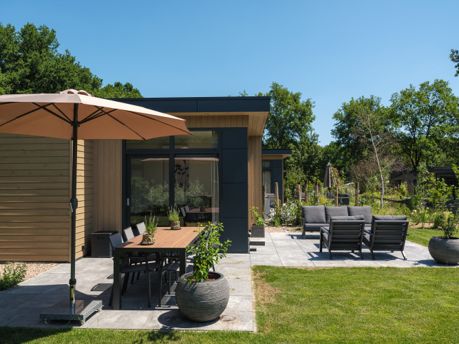 Moderne Lodge mit Terrasse, Gartenmöbeln und Sonnenschirm in Cannenburch, Veluwepark de Bosgraaf, Niederlande.