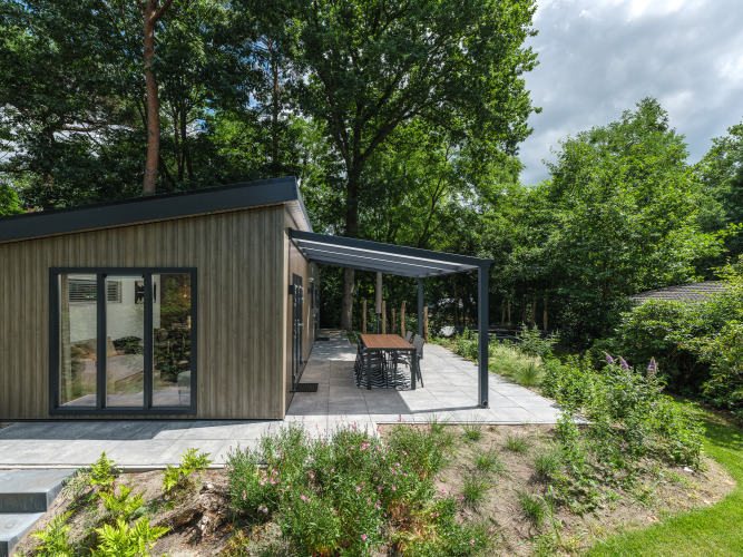 Außenansicht der Loevestein Deluxe-Lodge mit überdachter Terrasse im Veluwepark de Bosgraaf, Niederlande.