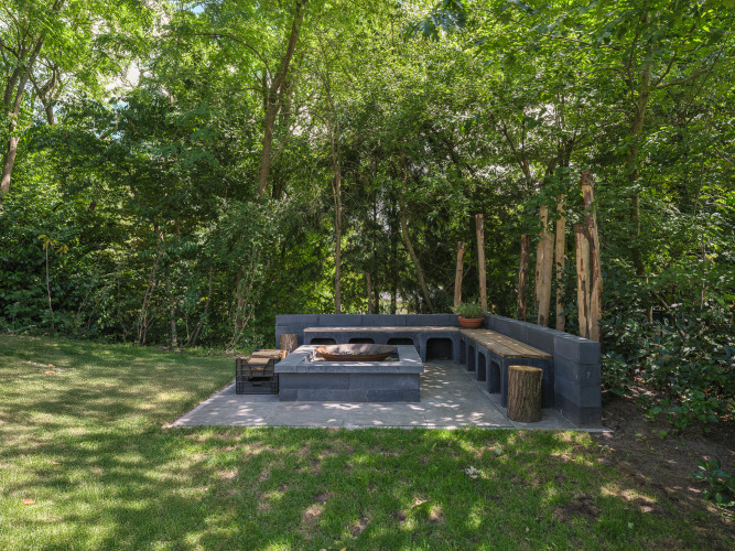 Gemütlicher Sitzbereich mit Feuerstelle und Bank im Loevestein Deluxe, Veluwepark de Bosgraaf, Niederlande.