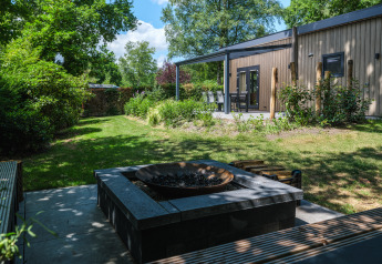 Gezellige zonnige tuin van Loevestein Deluxe lodge met houten gevel, terras en moderne vuurkorf.