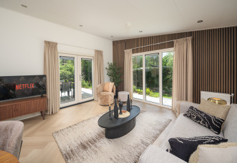 Moderne lodge woonkamer met grote ramen, beige gordijnen, houten muurpanelen en Netflix op de tv.