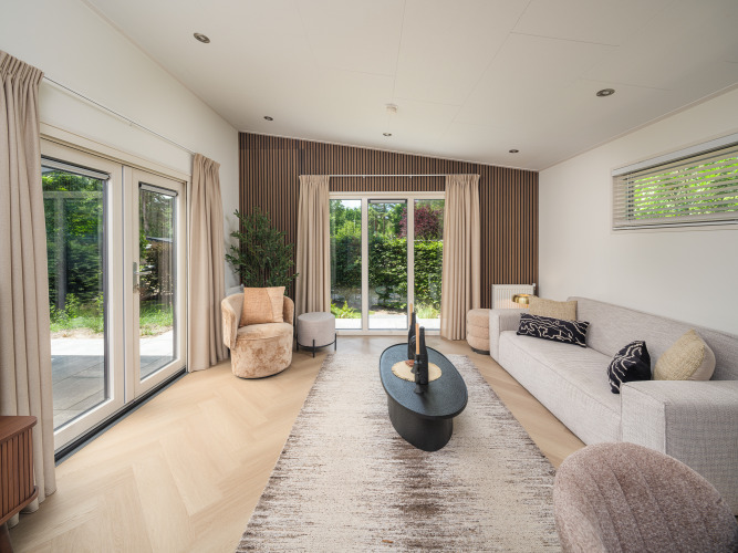 Modernes Wohnzimmer in einer Lodge mit großen Fenstern, heller Einrichtung, Vorhängen und Gartenblick.