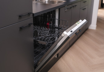 Lave-vaisselle intégré dans la cuisine moderne d’un lodge, porte ouverte et paniers vides apparents.