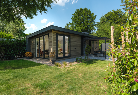 Moderne Zypendaal-lodge met grote ramen, terras en verzorgde tuin, omringd door bomen en struiken.