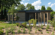 Moderne lodge met houten gevel en grote ramen, omringd door bomen en een groene voortuin.