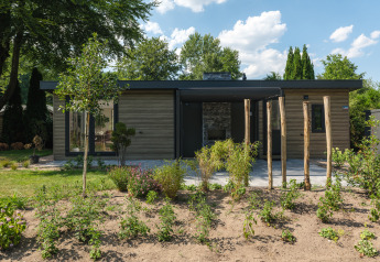 Lodge moderno con rivestimento in legno e grandi finestre, circondato da alberi e giardino anteriore.