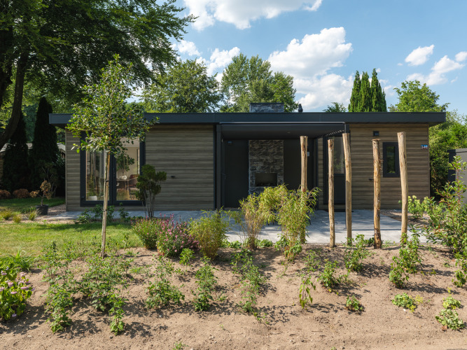 Moderne Lodge mit Holzfassade, großen Fenstern und gepflegtem Garten, umgeben von Bäumen und Himmel.