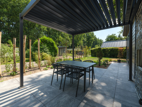 Udendørs terrasse ved en lodge med moderne pergola, havesæt og udsigt til grønne omgivelser.