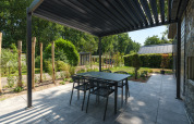 Terrasse extérieure d’un lodge avec pergola moderne, table à manger et chaises, jardin verdoyant autour.