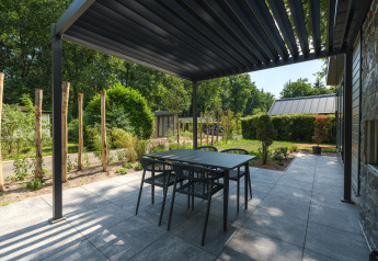 Terrasse extérieure d’un lodge avec pergola moderne, table à manger et chaises, jardin verdoyant autour.