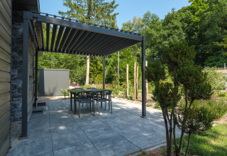 Modern patio with dining set and metal pergola at Zypendaal lodge, Veluwe park de Bosgraaf, Netherlands, amid greenery.