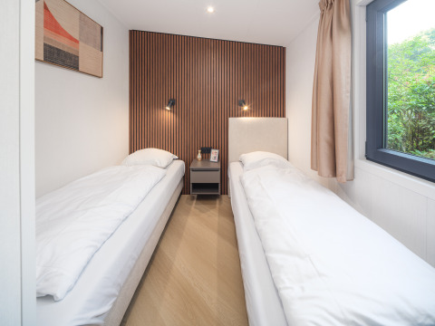 Chambre moderne avec deux lits simples et panneau en bois au Zypendaal lodge, Veluwepark de Bosgraaf, Pays-Bas.