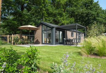 Lodge moderne entouré d'un jardin verdoyant, terrasse couverte, mobilier d’extérieur et grande nature.