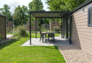 Terrasse d'un lodge moderne avec pergola, table et chaises, entourée de verdure et d'autres lodges voisins.