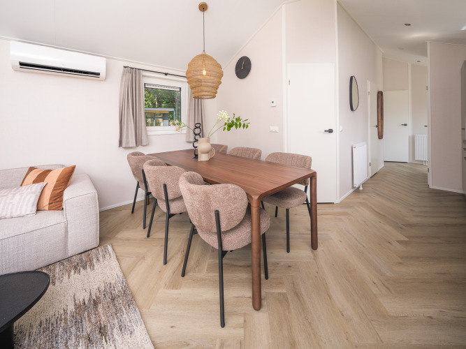 Moderne lodge spiseplads med træbord, seks polstrede stole, lyse trægulve og naturlig belysning.