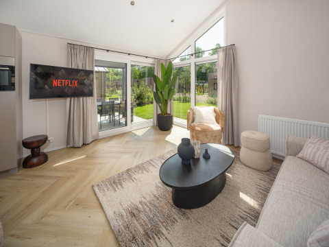 Moderne lodge woonkamer met bank, Netflix op TV, grote ramen, vloerkleed en uitzicht op de tuin.