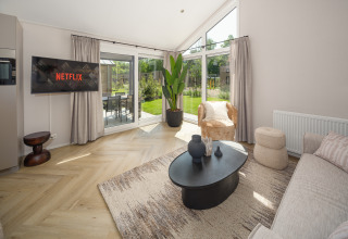 Moderne lodge woonkamer met bank, Netflix op TV, grote ramen, vloerkleed en uitzicht op de tuin.