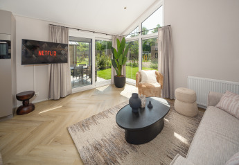Soggiorno moderno di un lodge con divano, TV con Netflix, grandi finestre, tappeto e vista giardino.