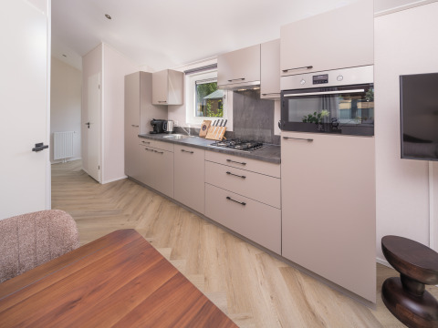 Moderne lodgekeuken met lichte kasten, ingebouwde apparatuur en houten eettafel bij daglicht.