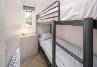 Kleines Lodge-Zimmer mit Etagenbett, Fenster, Heizung, einem Schrank und Lampe auf dem Schrank.