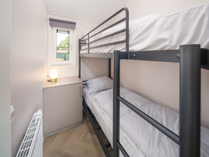 Kleines Lodge-Zimmer mit Etagenbett, Fenster, Heizung, einem Schrank und Lampe auf dem Schrank.