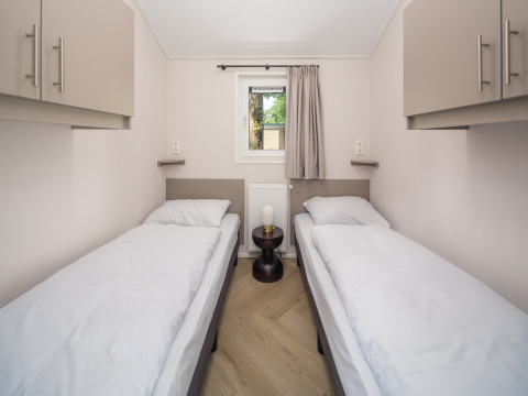 Een moderne lodgekamer met twee eenpersoonsbedden, witte beddengoed, bovenkasten en een klein tafeltje ertussen.