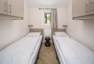 Een moderne lodgekamer met twee eenpersoonsbedden, witte beddengoed, bovenkasten en een klein tafeltje ertussen.