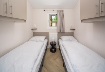 Habitación de cabaña moderna con dos camas individuales, ropa de cama blanca, armarios y una mesita central.