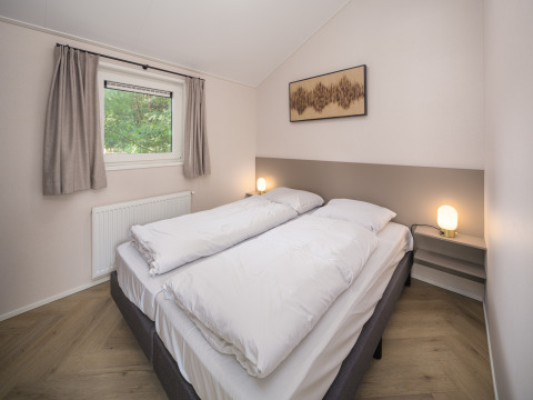 Lichte, moderne lodge-slaapkamer met tweepersoonsbed, witte dekbedden, lampen en raam met gordijnen.