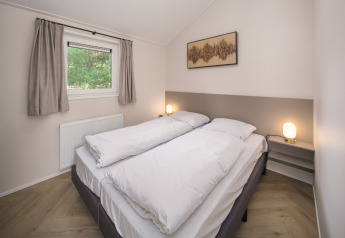 Dormitorio luminoso y moderno en una cabaña, con cama doble, edredones blancos y ventana con cortinas.
