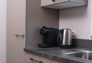 Kleine Küchenzeile mit Wasserkocher und Kaffeemaschine auf grauer Arbeitsplatte in einer Lodge.