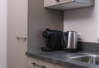 Pequeña cocina con hervidor eléctrico y cafetera sobre la encimera junto a un fregadero de acero en lodge.