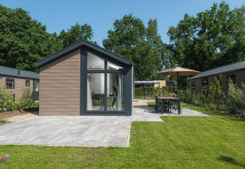 Modern Doornenburg Lodge featuring wood exterior, large windows, patio, and green lawn outdoors.