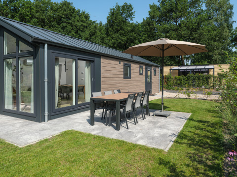 Moderne Doornenburg Lodge in Veluwepark de Bosgraaf met terras, eettafel, parasol en groene tuin.