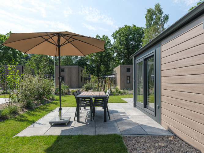 Terrasse bei Doornenburg Lodge im Veluwepark de Bosgraaf, Niederlande, mit Sonnenschirm und Möbeln.