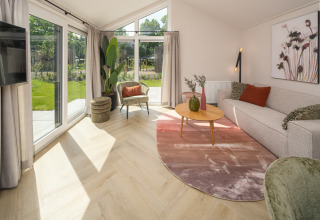 Salon lumineux à Doornenburg Lodge Comfort, Veluwepark de Bosgraaf, Pays-Bas, avec grandes fenêtres sur le jardin.