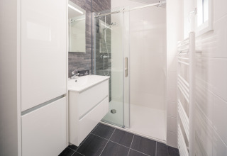 Moderne lodgebadkamer met een glazen douche, witte wastafel, kasten en donkere vloertegels.