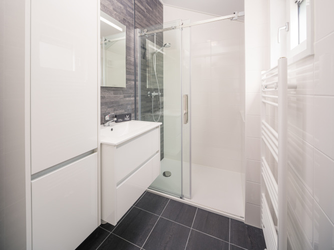 Modernes Lodge-Badezimmer mit Dusche, Glas-Schiebetüren, weißem Waschbecken und dunklen Fliesen.