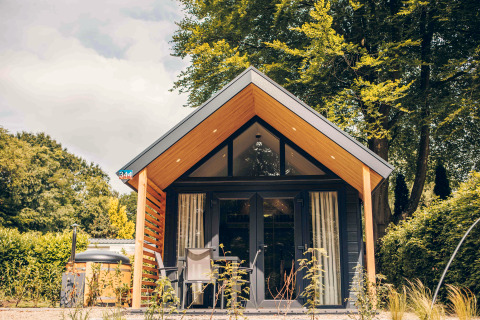 Tiny Loft tiny house with hot tub, modern wooden facade, surrounded by trees and sunny outdoor seating.