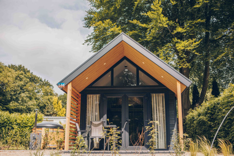 Tiny Loft tiny house with hot tub, modern wooden facade, surrounded by trees and sunny outdoor seating.